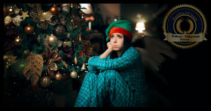 A girl sitting in front of Christmas tree wearing a Santa hat. She has a frown on her face. A Flourishing Life Society article on Holiday Depression
