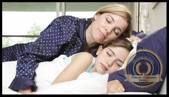 A woman warmly embracing her sleeping child. A Flourishing Life Society article on safe environments and personal growth